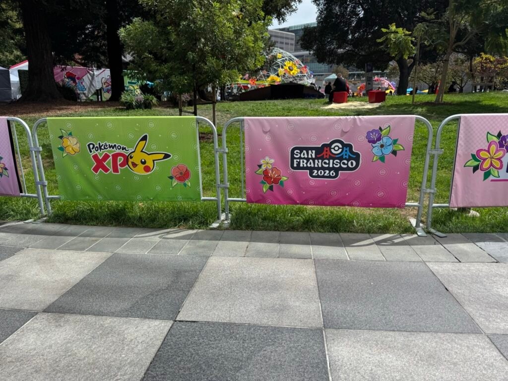屋外エリアの仮設フェンスに張られた花柄バナー。緑地に「Pokémon XP」とピカチュウ、ピンク地に「SAN FRANCISCO 2026」の文字と和柄の花があしらわれている