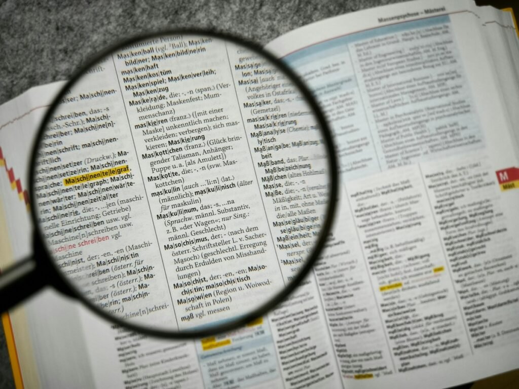 虫眼鏡で辞書のページを拡大したクローズアップ写真。単語の意味をひとつずつ丁寧に調べるイメージ