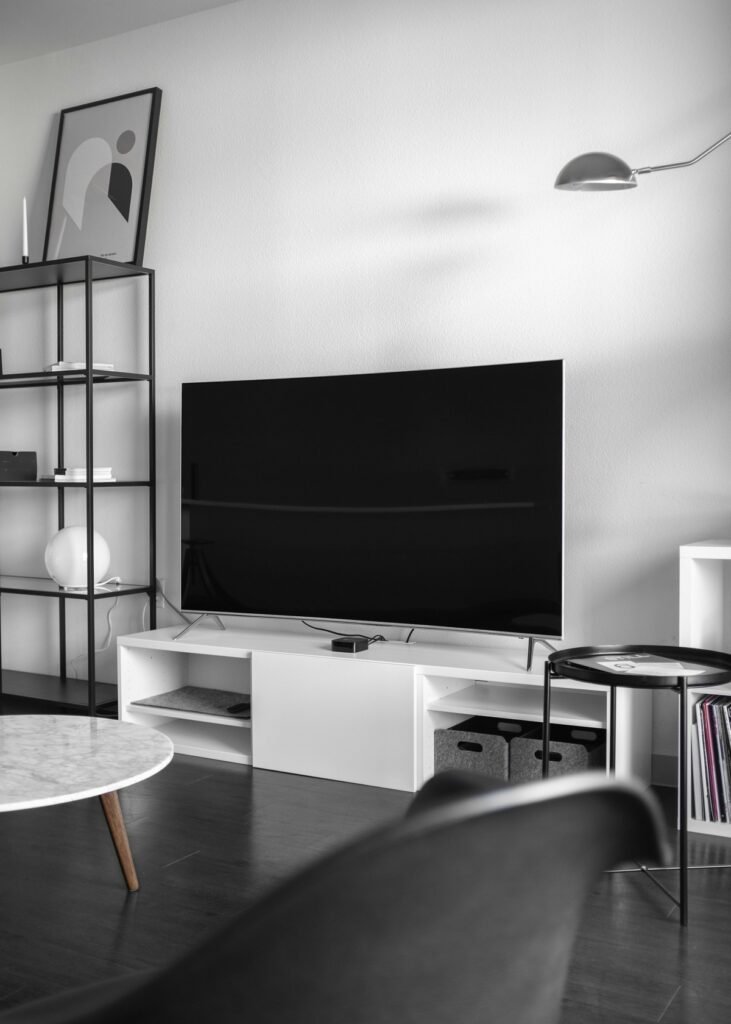 白いテレビ台に置かれた大型テレビと、手前の汎用的な黒い小型ストリーミング機器。外付け機器でスマート機能を補うイメージ写真