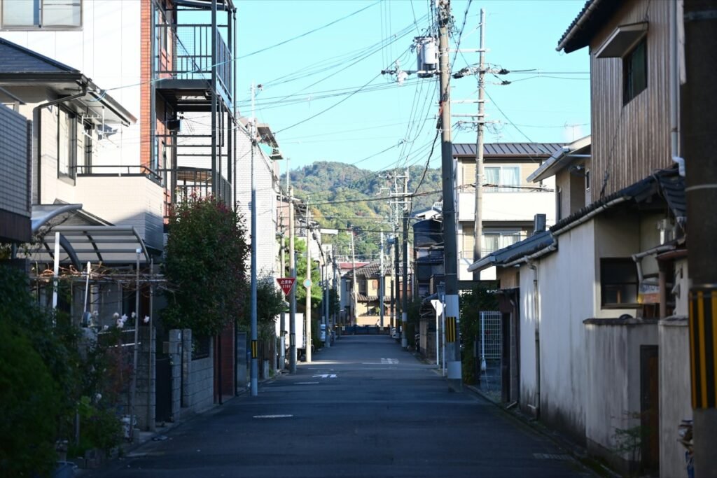 日本の街のイメージ。電柱と電線が並び「止まれ」標識が立つ京都の静かな住宅街の一本道と、奥に見える緑の山(素材写真)