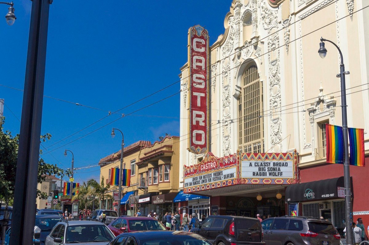 サンフランシスコ・カストロ地区のカストロ劇場（Castro Theatre）。赤い「CASTRO」の縦型看板と、街灯に掲げられたレインボーフラッグが並ぶ晴れた日のCastro Street（素材写真）